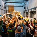 A large group of people collectively holding up a sculpture made of cardboard and paper