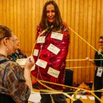 A person wrapped up in red transparent paper with post-it notes stuck on her that read 'Have babies' and 'Grow own food'