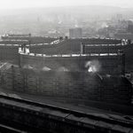 A black and white photo taken from a high vantage point of a large brutalist building with lots of windows. It is foggy.