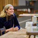 Alison Oliver sits at a table in a blue velvet top.