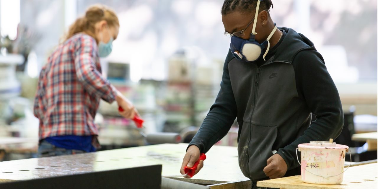 Scenic art apprentice painting, wearing mask.