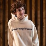 Archie Barnes, standing and smiling looking off to the right, wearing an off-white hoodie with 'GoodThingsToCome' written across the chest.