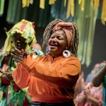 A cast member dressed in orange smiling and clapping