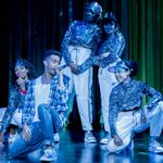 A group of five actors, dressed in sparkly outfits and visors, singing and posing