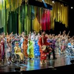 The As You Like It company onstage dressed in multicolours