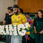 The cast rehearsing Hamlet, carrrying a floral wreath spelling the word KING.