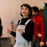 Claire Redcliffe, wearing a blck top and denim dungarees, and other cast members rehearsing Hamlet for younger audiences