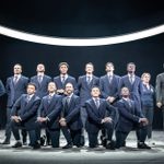 A group of men and one woman pose for a team photograph. most wearing blue suits, one man wearing shorts and England tracksuit top, another man, older than the rest, wears a black suit.The woman wears an England tracksuit.