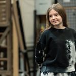 A teenage girl with light brown hair, wearing a tie-dye black and white jumper.