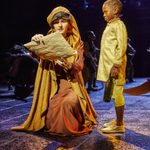 A kneeling woman holds a script next to a young boy.