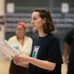 A woman stands holding a script.