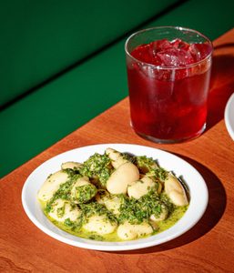 A plate of braised butter beans with Salsa Verde, with a Cherry Negroni cocktail.