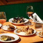 On a table, a selection of Italian dishes and glasses filled with wine are spread out.