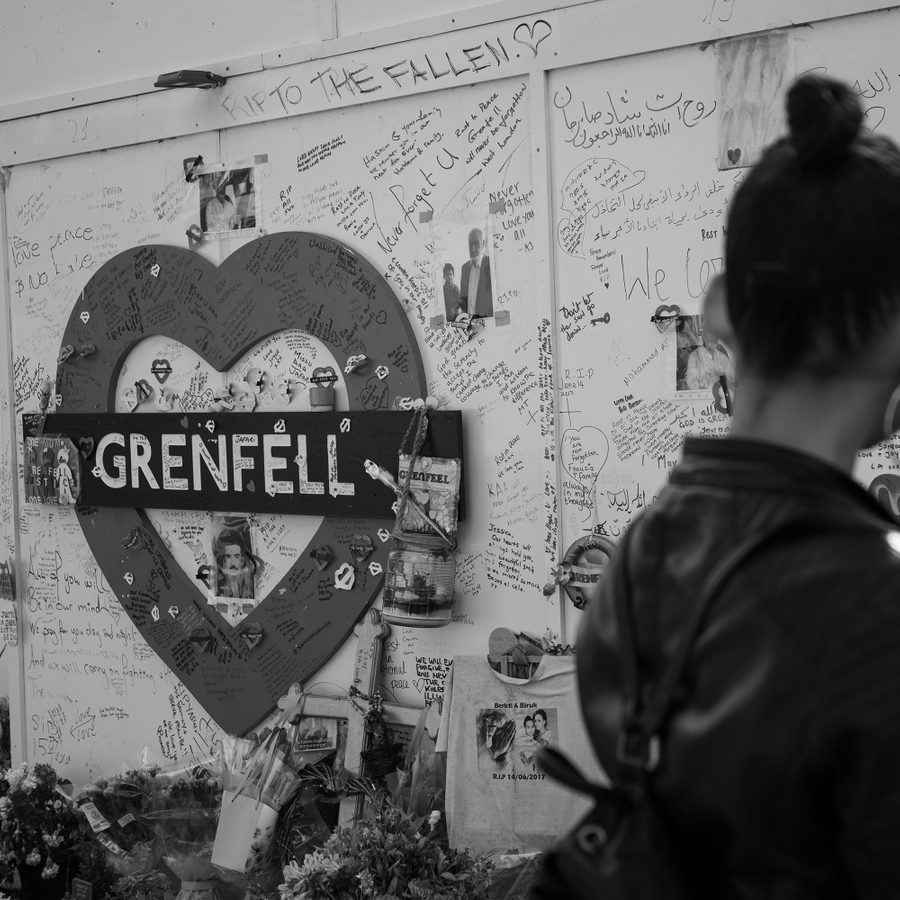 A mural of a heart-shaped tube sign with the words 'Grenfell' has been covered with messages for the bereaved. A woman stands silhouetted in the foreground, slightly out of focus.