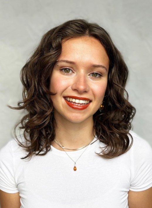 A photograph of a young person with long brown, wavy hair and wearing red lipstick