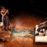 Two people sat on wooden chairs on raised wooden daises opposite one another, with blue rope tangled between them