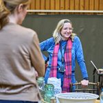 Josie Rourke leans against a chair in a blue jumper and pink scarf.