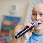 Kathrine Payne, in a blue sleeveless top and speaking into a microphone, rehearsing Hamlet for younger audiences.