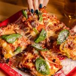 A close up of people's hands picking up three pieces of pizza, leaving a fourth piece on a tray.