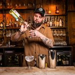 A barman mixing drinks with shelves of bottles behind him