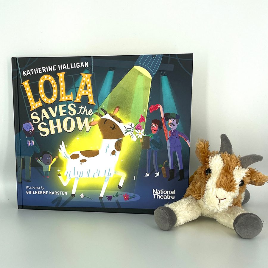 The children's picture book 'Lola saves the show' sitting on a grey table, with a cuddly toy of a goat sitting next to it.