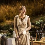 Louisa Harland as Agnes standing and smiling wearing a long beige dress.