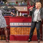 Two women in a karaoke session, one with a microphone and the other danncing, in a cafe/diner