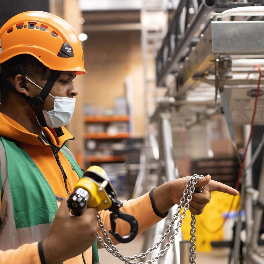 A Young Technician in an orange hard hat holding a piece of rigging