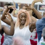 Focus in on an individual during rehearsal, smiling with their arms in the air.