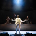 Actor Ashley Zhangazha, dressed all in white, standing downstage singing with his arms wide open