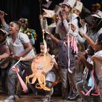 A group of young people in the community cast costumed in hats and animal outfits, all with streamers.