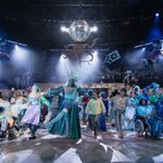 The cast dancing together onstage, dressed in an array of blue sparkly outfits.