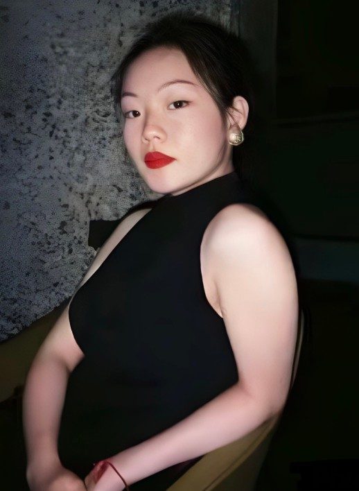 A photograph of a person wearing a sleeveless black top with black hair and red lipstick