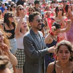 A group of vibrant and diverse people in summer attire at an outdoor event. They are dancing, smiling, cheering, and clapping.