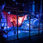 Blue and red transparent fabric being held up by cast members through light.