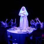 A bride stands on a table surrounded by people illuminated by blue light in a moment of solitude