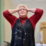 Siobhán McSweeney with her hands pressed to her forehead in a red shirt and black jumpsuit.