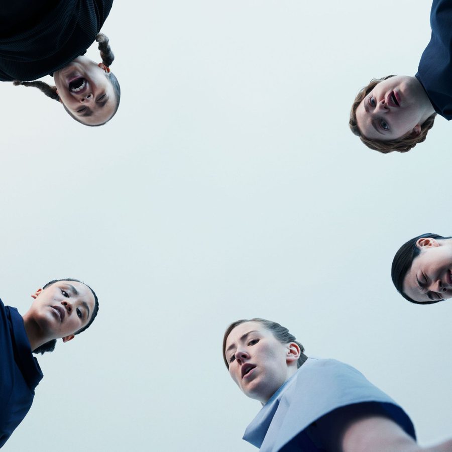 The Crucible - the heads and shoulders of two young women, looking down with an overcast sky above