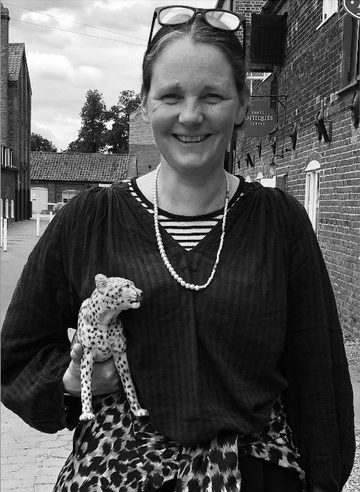 A black and white photo of a person smiling wearing a black cardigan and carrying a leopard toy