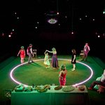 A stage in the round, grass turf of the floor with an illuminated circle.