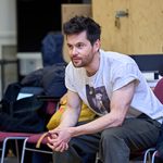 Tom Riley sitting in a chair in a white t-shirt.