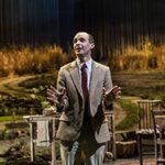 Tom Vaughan-Lawlor as Michael standing in a grey suit.