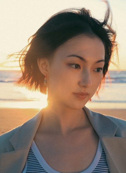 A person with black hair in a bob haircut, standing against a sunset on the beach